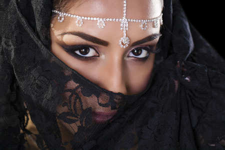 Portrait of a beautiful woman with arabian makeup in black paranja isolated on dark backgroundの写真素材