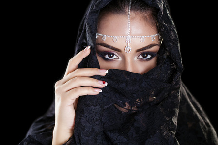 Portrait of a beautiful woman with arabian makeup in black paranja isolated on dark backgroundの写真素材