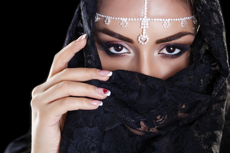 Portrait of a beautiful woman with arabian makeup in black paranja isolated on dark backgroundの写真素材