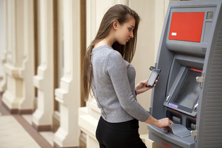 Young brunette woman withdrawing money from credit card at ATMの写真素材