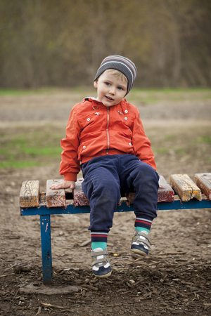 Full length portrait of a beautiful baby boy walking in spring park. Little boy in orange jaket and blue jeans, outdoorsの写真素材