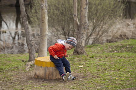 Little boy sitting on a stump in the spring park. Baby boy in orange ja?ket, outdoorsの写真素材