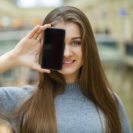 Young brunette woman covers her face screen smart phone, indoorの写真素材