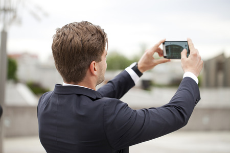 Young business man taking pictures on a mobile phone, summer street outdoorsの写真素材