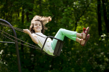 Happy Little girl on a swing in the summer parkの写真素材