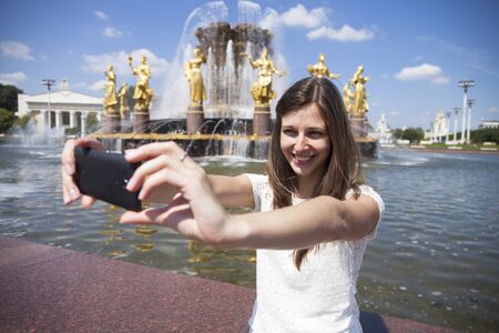 Beautiful, smiling brunette woman take a picture of herself with a smartphone. selfie, summer outdoorsの写真素材
