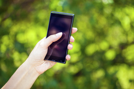 Side view of a woman's hand holding a modern slick smartphone while dialing with her thumb against...