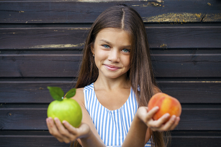 Little girl holding a green apple and a peach, summer outdoorsの写真素材