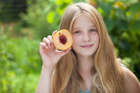 Portrait of a young blonde little girl with peach, summer outdoorの写真素材