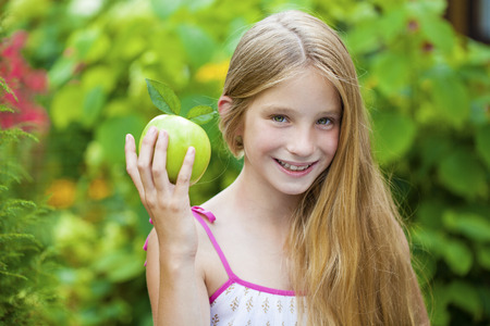Happy blonde little girl with green apple, summer outdoorsの写真素材