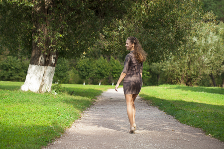 Portrait in full growth, young beautiful brunette woman in brown dress walking in the summer parkの写真素材