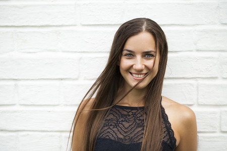 Closeup portrait of a happy young woman smiling, against a white brick wall, summer outdoorsの写真素材