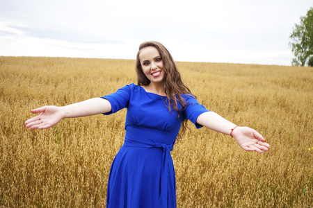 Portrait of a young brunette woman on a background of golden wheat field, summer outdoorsの写真素材
