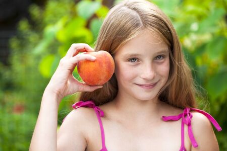 Portrait of a young blonde little girl with peach, summer outdoorの写真素材
