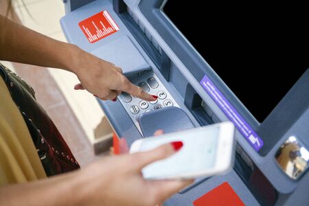 Close up of hand entering pin at an ATM. Finger about to press a pin code on a pad. Security code on an Automated Teller Machine. Female arms, ATM - entering pinの写真素材