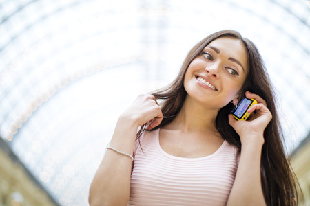 Young beautiful brunette woman in pink dress calling on a cell phone, posing against a background of...