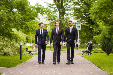 Three young men in elegant business suits walking in summer street, outdoorsの写真素材