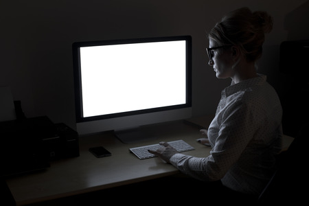 Overtime in the office. A young woman working at the computer late at nightの写真素材