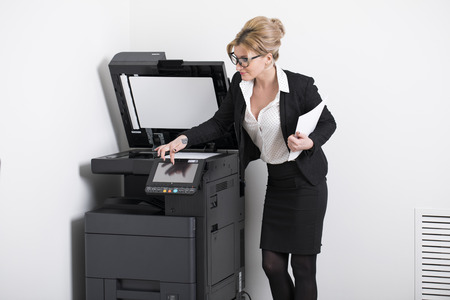 Young beautiful woman in a black polka-dot dress making copies in the officeの写真素材