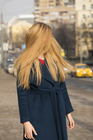 Portrait of a young beautiful blonde woman in blue coat on a background of spring streeteetの写真素材