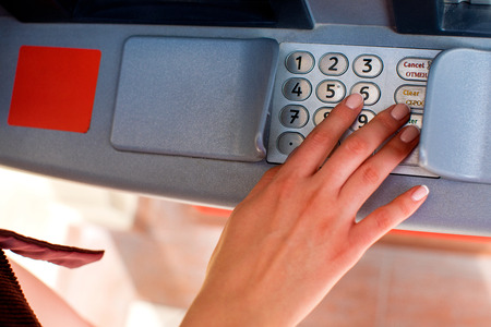 Close up of hand entering pin at an ATM. Finger about to press a pin code on a pad. Security code on...