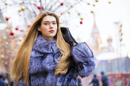 Portrait of a beautiful young blonde woman in a blue fur coat, winter street outdoorsの写真素材