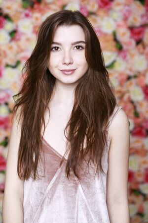 Closeup portrait of a beautiful young brunette girl in a studio on a floral wall background