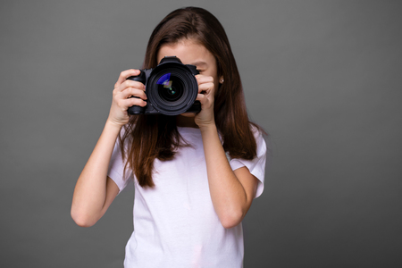 Cute brunette little girl holding an photo camera, isolated on gray backgroundの写真素材