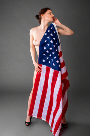 Full portrait of sexy naked woman holding a large American flag, isolated on dark gray backgroundの写真素材