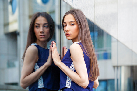 Portrait close up of young beautiful brunette woman in blue dress posing near mirrored wallの写真素材