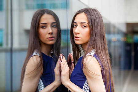 Portrait close up of young beautiful brunette woman in blue dress posing near mirrored wallの写真素材