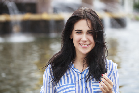 Happy young brunette woman in a striped blue shirt, on summer park backgroundの写真素材
