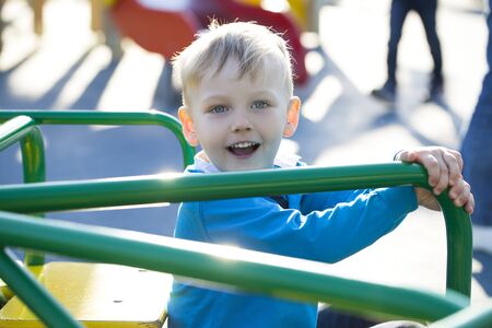 Portrait of a young blonde boy sitting on a carousel at the playgroundの写真素材