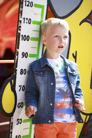 Restrictions on growth in a childrens amusement park, A five year old boy stands against the background of a mans growth lineの写真素材