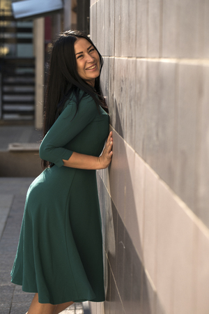 Close up portrait of beautiful young happy brunette woman in green dress, street summer outdoorsの写真素材