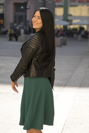 Portrait of a beautiful young brunette woman in green dress on a background of summer streetの写真素材