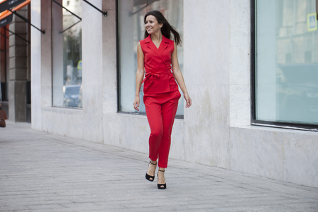 Portrait in full growth of a beautiful young woman in red suit, street summer outdoorsの写真素材