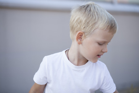 Blonde Little boy in a white T-shirt on a street backgroundの写真素材