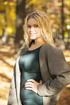 Portrait of a young beautiful blonde woman in gray coat on a background of autumn streetの写真素材