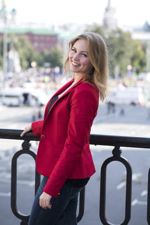 Portrait close up of young beautiful happy blonde woman in red jacket, summer street outdoorsの写真素材