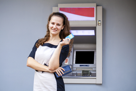 Young happy brunette woman withdrawing money from credit card at ATM の写真素材