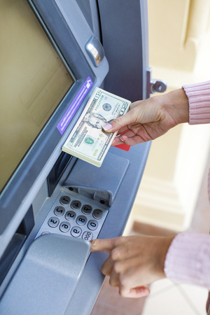 Young beautiful blonde woman is holding a cash dollars on the background of the ATM in a shopping centerの写真素材