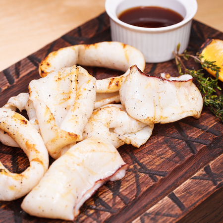 Restaurant dish - grilled squid rings on a wooden board with sauceの写真素材