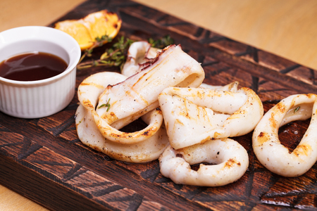 Restaurant dish - grilled squid rings on a wooden board with sauceの写真素材