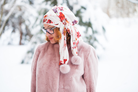 An adult beautiful woman in a fur coat posing against the background of a snow-covered winter parkの写真素材