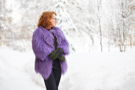 Adult beautiful woman in llama fur coat posing against the background of a snow-covered winter parkの写真素材