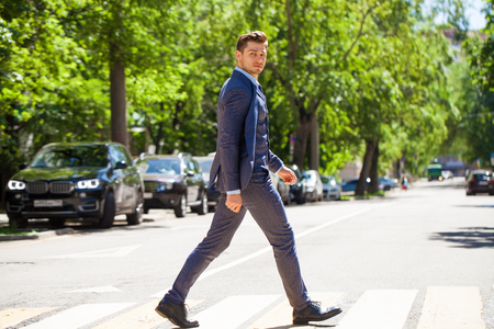 Portrait in full growth of a young man in a business suit crosses the road on a pedestrian crossingの写真素材
