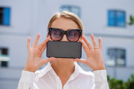 Young beautiful blonde woman showing your smartphone screen, summer park outdoorsの写真素材