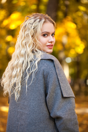 Portrait of a young beautiful blonde woman in gray coat on a background of autumn streetの写真素材