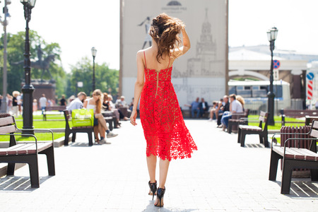 Back view, young brunette woman in summer red dress on street backgroundの写真素材
